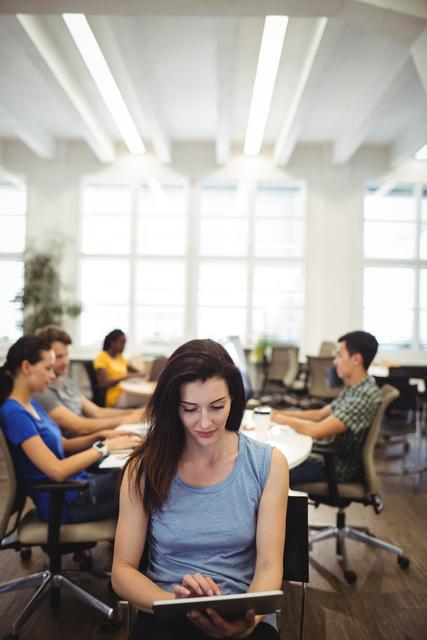 Woman Using Tablet in Modern Office Setting with Colleagues Working - Download Free Stock Images Pikwizard.com