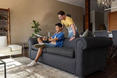 Two friends reading documents on dark gray sofa in open-plan living room, casual teamwork