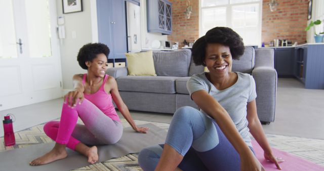 Happy african american mother and daughter doing yoga in living room, stretching. domestic life and quality family time together at home.