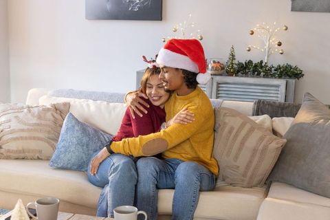 Couple hugging on couch celebrating cozy christmas wearing santa hat and festive sweaters
