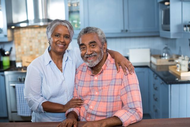 Senior couple embracing in home kitchen, smiling at camera. Great for representing retirement life, family bonds, and domestic happiness. Suitable for articles on aging, relationships, and healthy lifestyles.