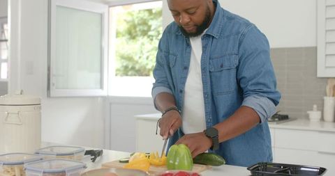 Man chopping yellow bell pepper on kitchen island preparing healthy meal in sunlit modern kitchen