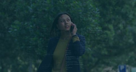 Professional woman walking and talking on smartphone with code overlay urban park backdrop