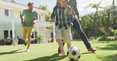 Multi-generational family playing soccer in sunlit garden