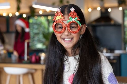 Smiling indian girl wearing glittery christmas tree glasses during home holiday celebration