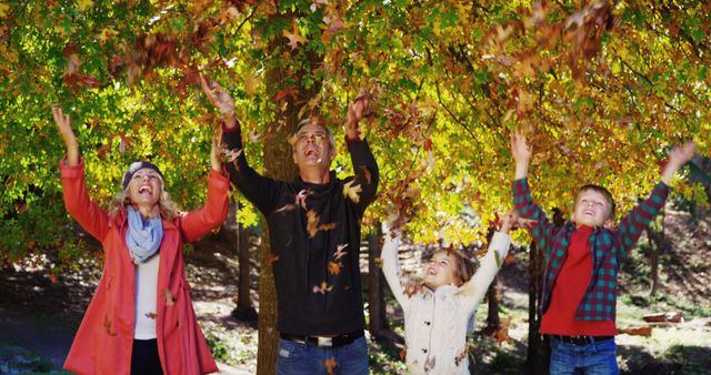 Happy family of four enjoying an autumn day. The parents and children are seen throwing colorful leaves in air, smiling and having fun in forest. Applicable for topics on family bonding, outdoor activities, autumn celebrations, and nature. Great for illustrating joyful moments, seasonal change content, and advertisements promoting family experiences.