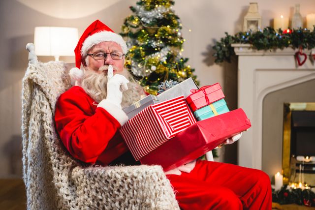 Santa claus with gift boxs sitting on chair with finger on lips in living room during christmas time