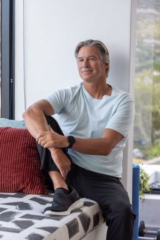 Mature man relaxing on window bench gazing at hills with smartwatch and workout gear