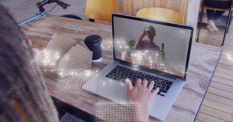 Typing on laptop during remote video call with digital data overlay in cafe workspace