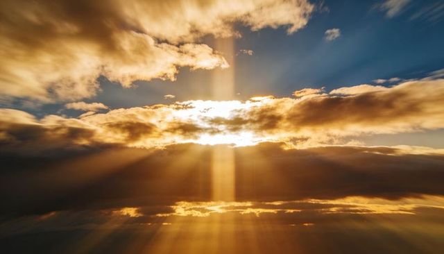 Golden sunbeams piercing layered clouds at sunrise, dramatic crepuscular rays across sky