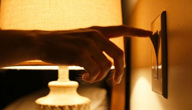 Hand Reaching to Turn Bedside Lamp Switch, Warm Ambient Glow and Intimate Night Scene