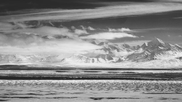 Scenic view of Arctic landscape in monochrome featuring dramatic clouds and snow-capped mountains. Ideal for projects emphasizing natural beauty, solitude, or harsh climates. Perfect for travel brochures, environmental campaigns, or prints for nature enthusiasts.