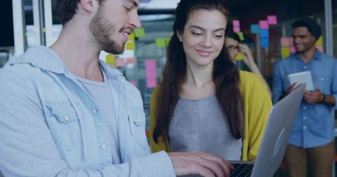 Young professionals collaborating over laptop brainstorming with colorful sticky notes on glass