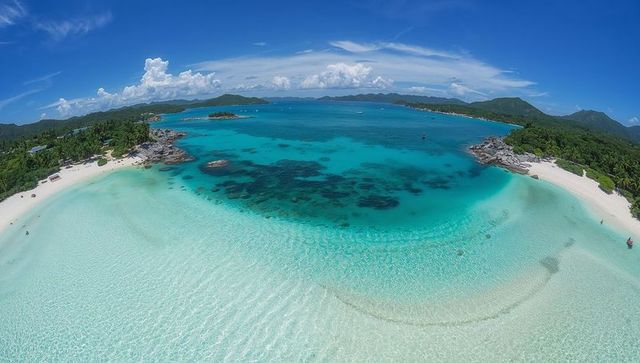 Turquoise crescent lagoon unfolding over white sand beaches, palm-lined island bay