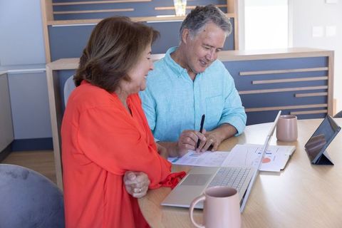 Mature couple reviewing retirement finances at kitchen table with laptop and charts