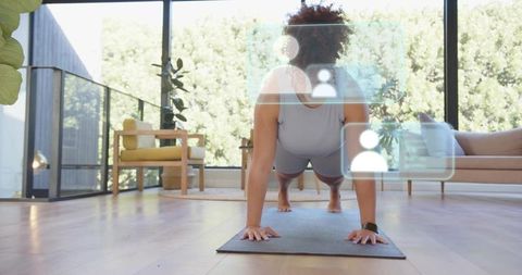 Woman holding high plank during home workout on yoga mat with smartwatch and hud in sunlit living ro