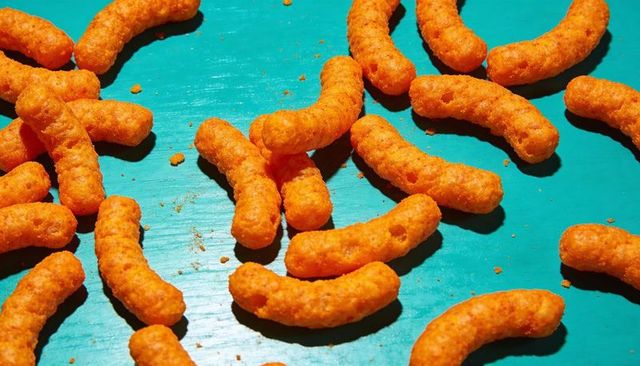Bright orange cheese puffs scattering on turquoise wooden board showing crunchy snack texture