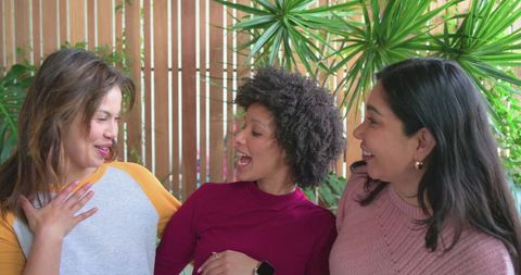 Diverse women laughing and chatting on sunlit porch wearing smartwatch and gold hoop earrings