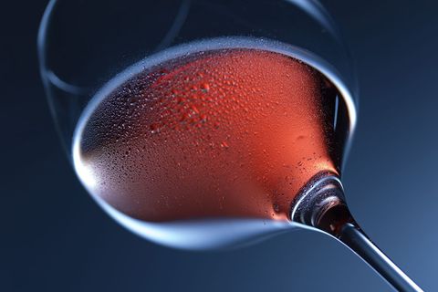 Tilting glass revealing chilled rosé with dewy droplets on moody blue background
