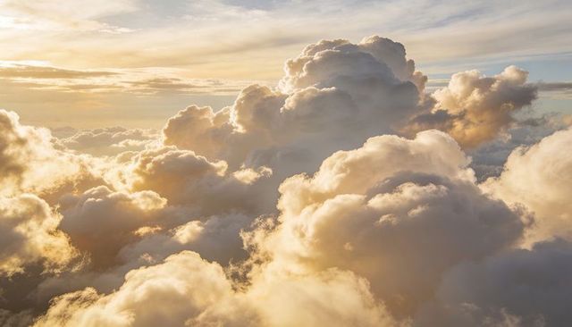 Golden hour cloudscape with towering cumulus, sunlit rays, ethereal sky for backgrounds