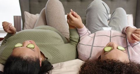 African American Friends Relaxing with Cucumber Eye Masks Holding Hands on Bed