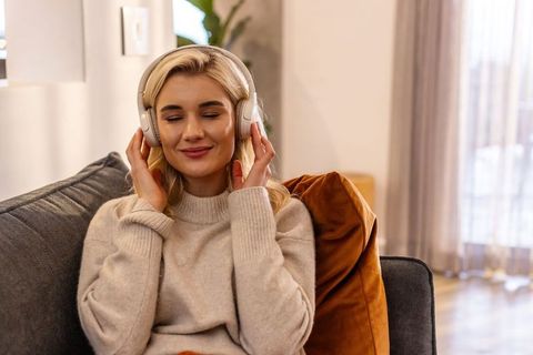 Young woman listening to music on wireless headphones on cozy living room sofa