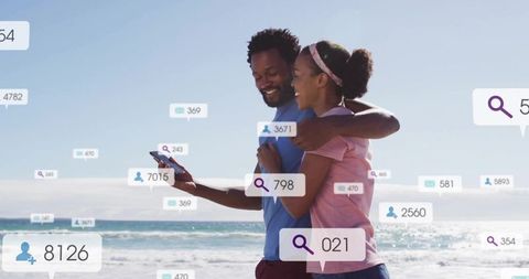 Couple embracing on beach checking social media engagement overlays on smartphone