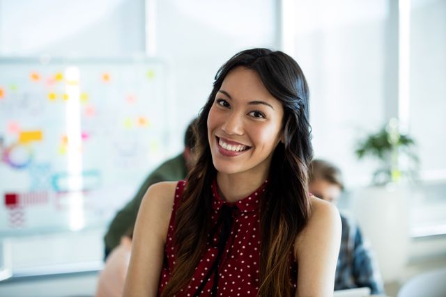 Young woman smiling in a modern office environment. Ideal for business, professional, and workplace themes. Perfect for illustrating positive work culture, teamwork, and success in corporate settings.