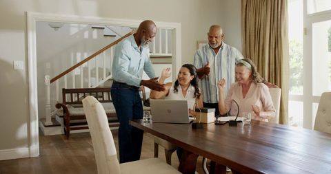 Multigenerational diverse family celebrating around laptop on sunlit dining table
