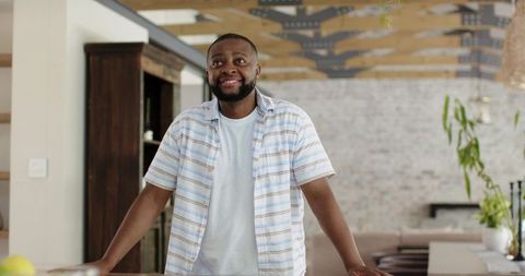 Smiling man leaning on kitchen counter in modern open-plan home with wood and brick accents