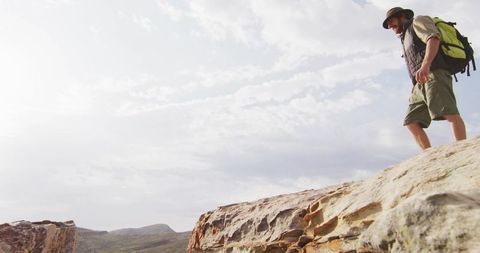 Hiker standing on rocky outcrop overlooking canyon with backpack and sunhat