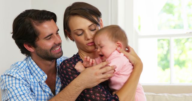 A young Caucasian couple is comforting their crying baby at home, with copy space. Their expressions convey concern and care as they try to soothe their infant.
