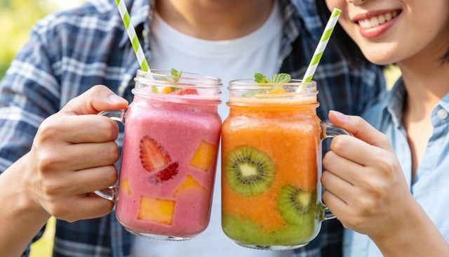 Couple clinking mason jars holding strawberry-mango and kiwi smoothies outdoors