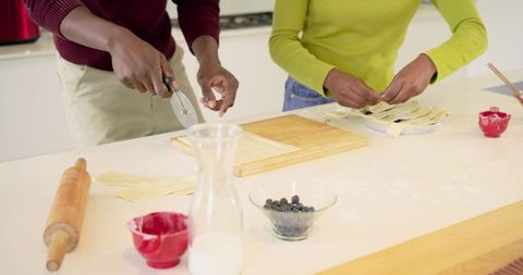 Couple weaving pastry lattice on kitchen island, cutting dough and preparing blueberry pie