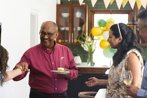 Senior man celebrating birthday with family in decorated kitchen holding cupcake candle