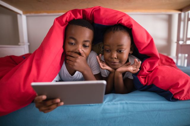 Surprised siblings holding digital tablet while lying on bed at home