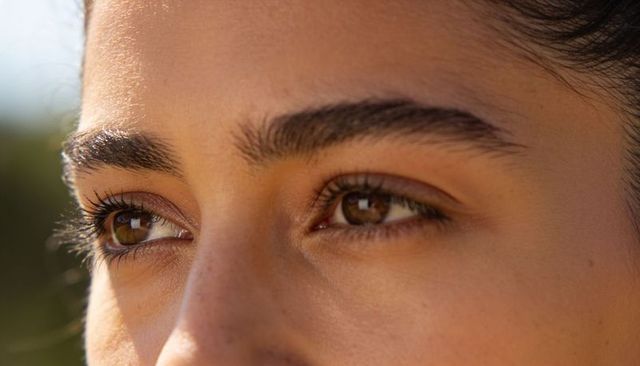 Gazing young woman with brown irises and full eyebrows in warm golden sunlight closeup