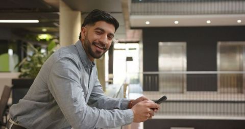 Young Professional Smiling Checking Smartphone in Urban Office Atrium