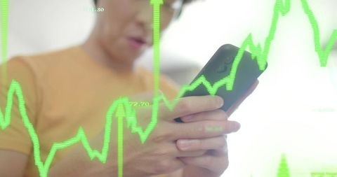 Asian man holding smartphone analyzing neon green stock chart overlay on mobile device