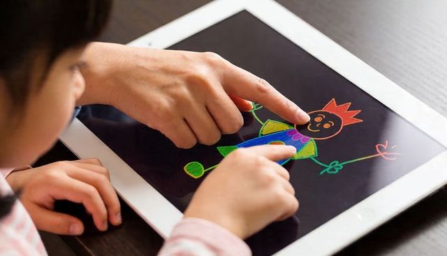 Parent guiding child creating colorful finger-paint drawing on tablet for learning