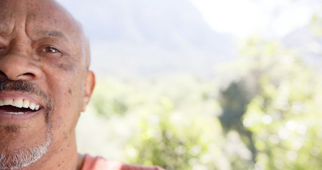 Half portrait of happy bald senior african american man in sunny nature, copy space, slow motion. Summer, retirement, wellbeing and healthy senior lifestyle, unaltered.