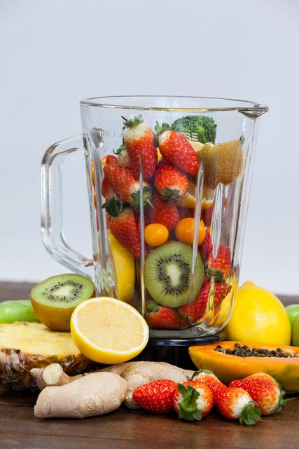 Various fresh fruits and vegetables are arranged inside and around a blender on a wooden table. This image highlights the concept of a healthy diet and clean eating. Excellent for use in articles, blogs, or advertisements related to nutrition, wellness, detox recipes, and fitness.