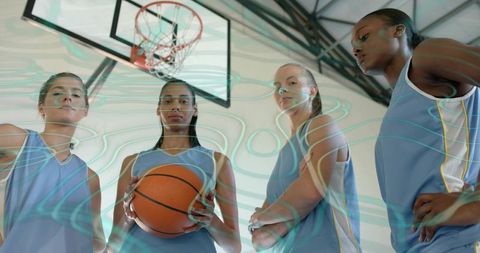Young women basketball team standing united under hoop holding ball, focused teamwork