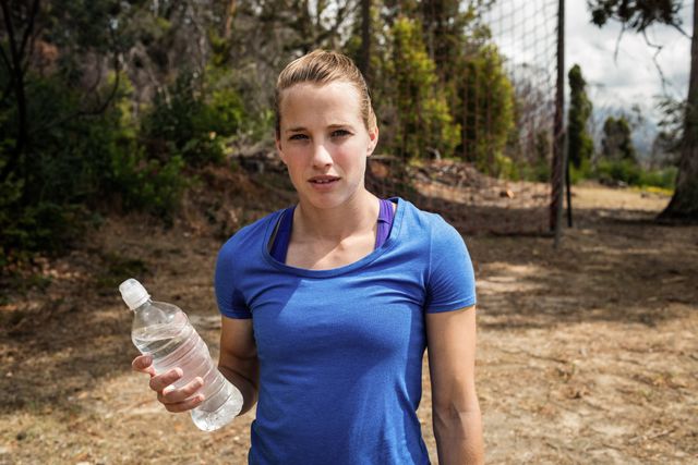 Fit woman holding a water bottle during an outdoor boot camp. Ideal for promoting fitness, healthy lifestyle, hydration, and outdoor activities. Suitable for use in fitness blogs, health and wellness websites, and exercise-related advertisements.