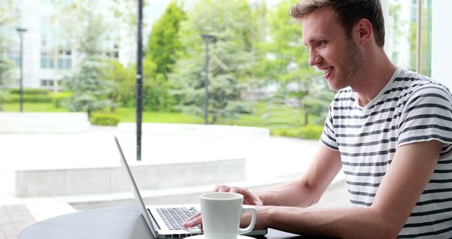 Smiling Man in Striped Shirt Working on Laptop at Cafe - Download Free Stock Images Pikwizard.com