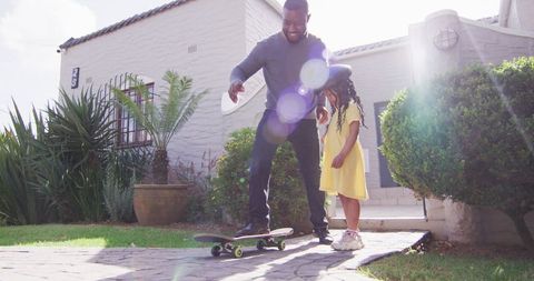 Father Teaches Daughter Skateboarding in Sunny Backyard