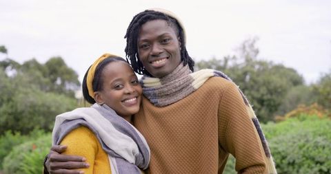 Smiling african american couple embracing in lush garden wearing cozy sweaters and scarves