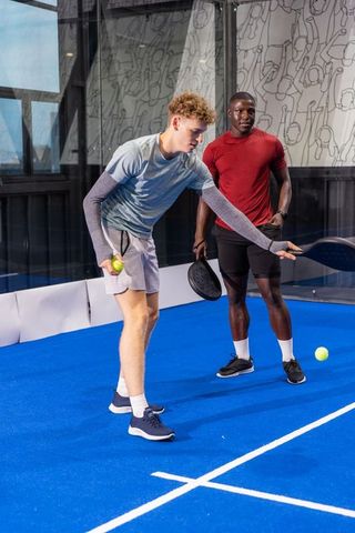 Diverse young men practicing paddle serve and training on bright blue indoor glass court