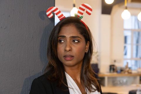Indian businesswoman wearing candy cane headband leaning on grey wall in coworking office