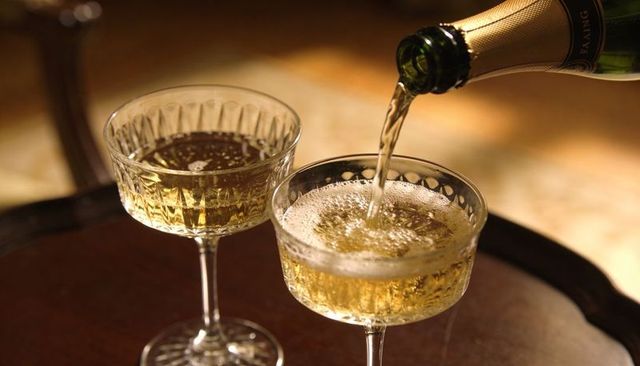 Pouring champagne into cut-crystal coupes on wooden tray, golden bubbles and foam